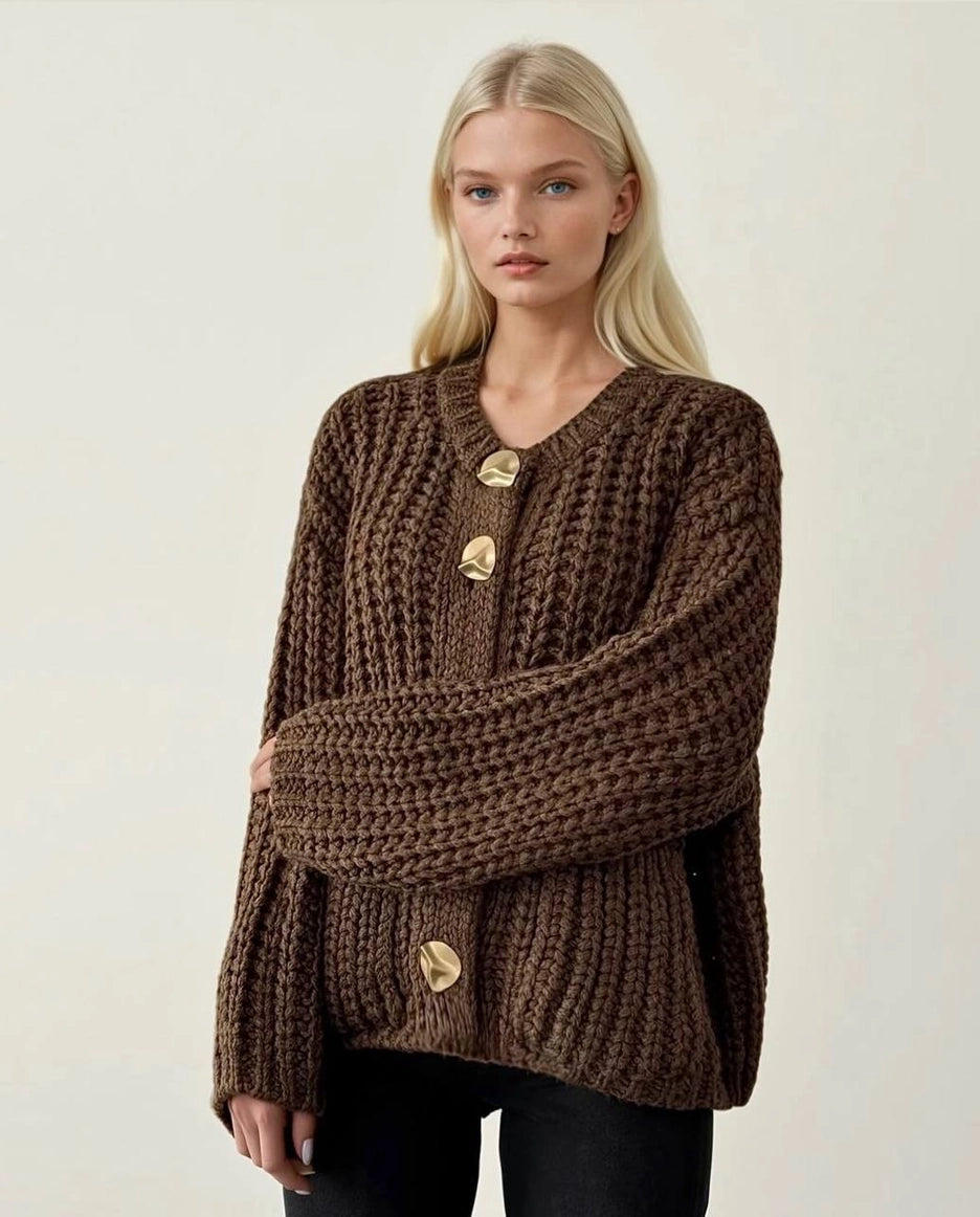 Woman wearing a brown knitted sweater with gold buttons on a plain background ANAZ