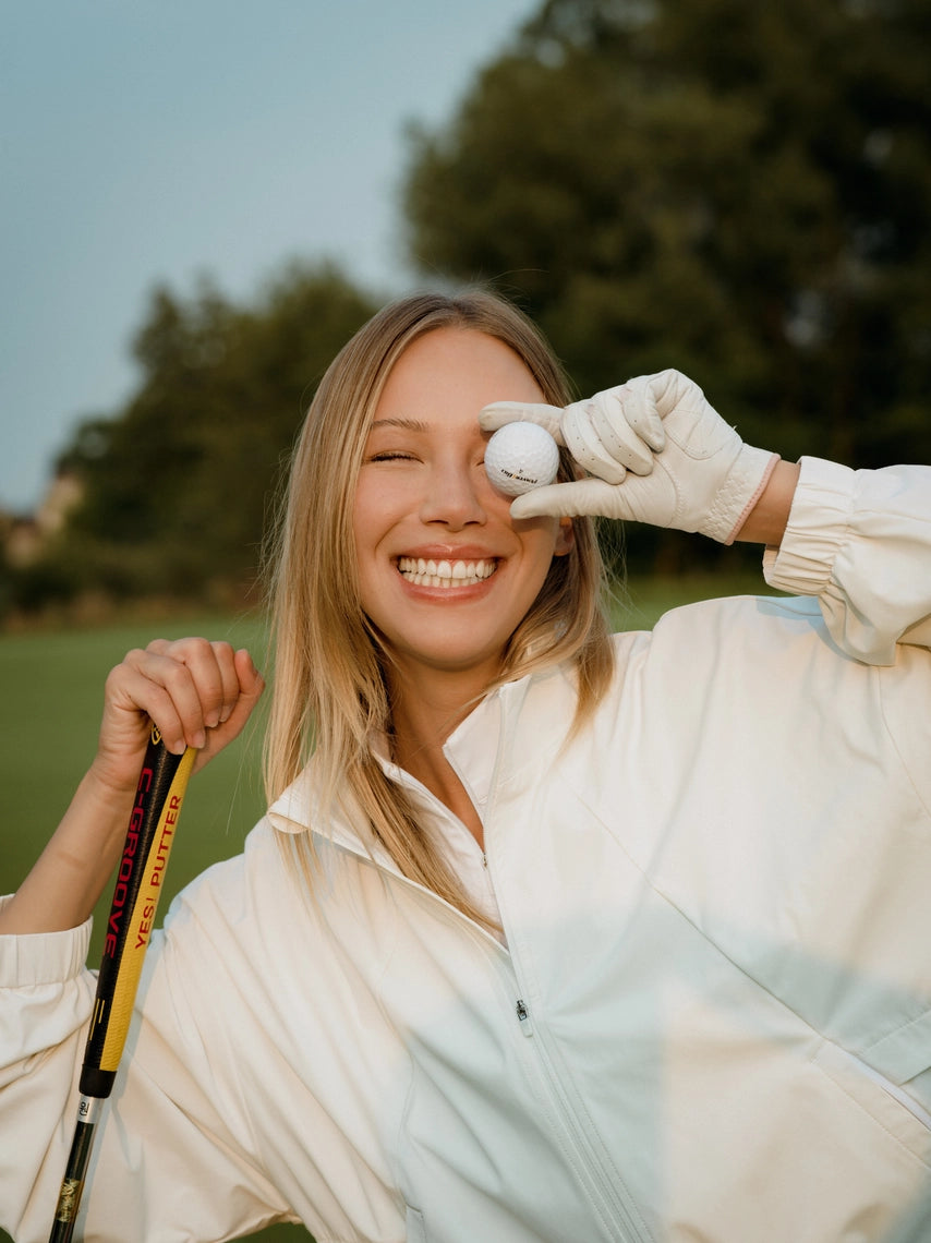 Woman holding a golf club and a golf ball on a golf course
