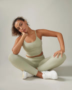 Woman in a green athletic outfit sitting on the floor against a plain background Rose Boreal