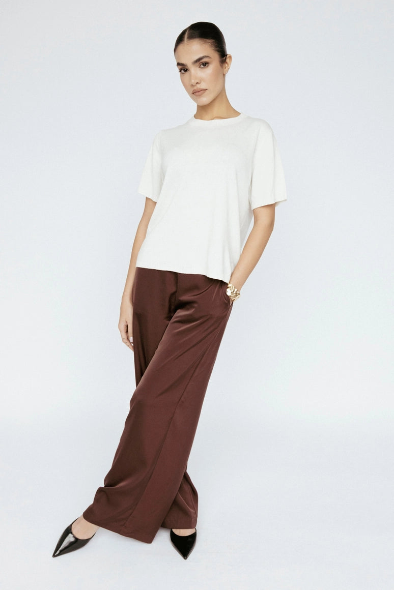 Woman wearing a white top and brown pants on a white background Amanda Maria