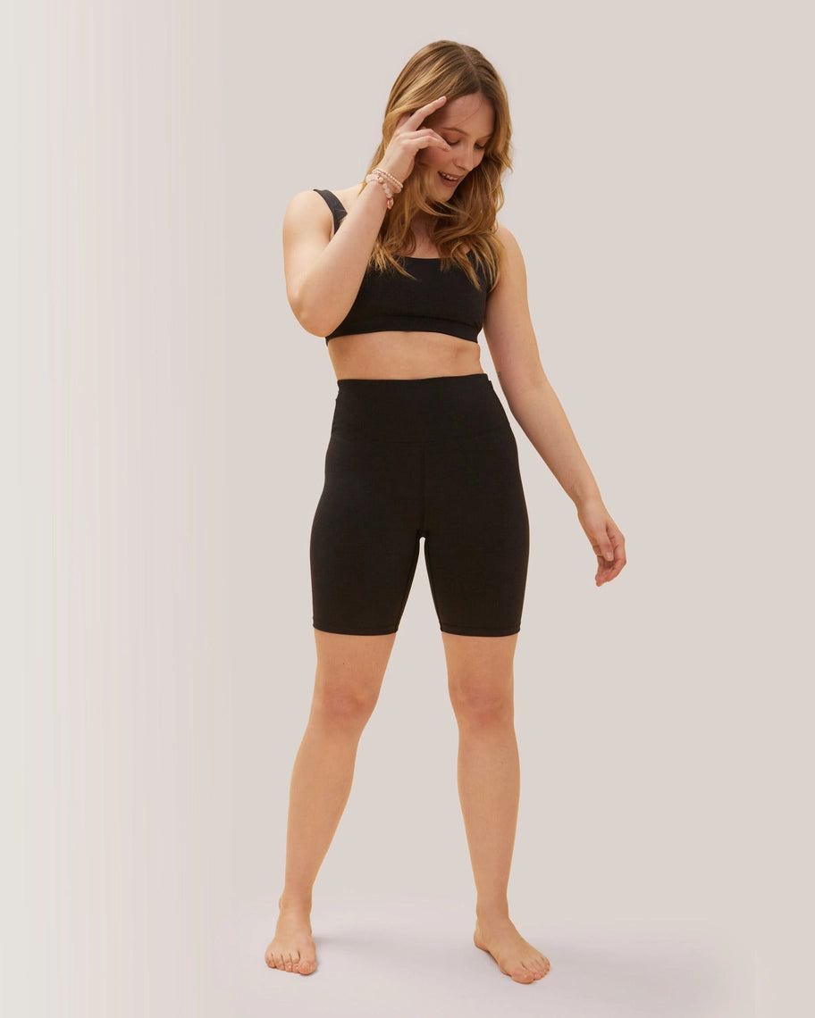 Woman wearing a black sports bra and high-waisted shorts on a plain background Rose Boreal