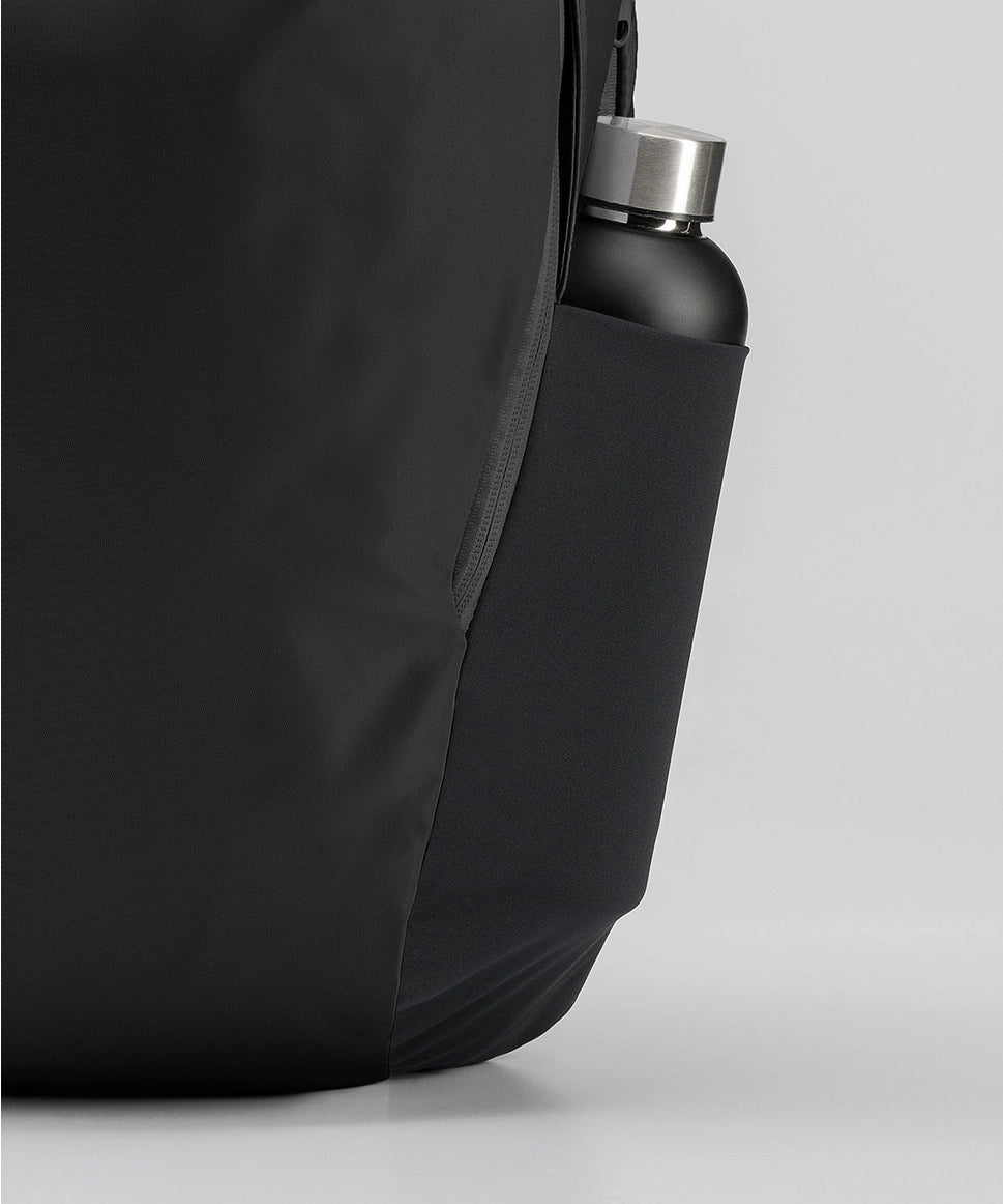 Black backpack with a water bottle in a pocket on a light gray background RYU