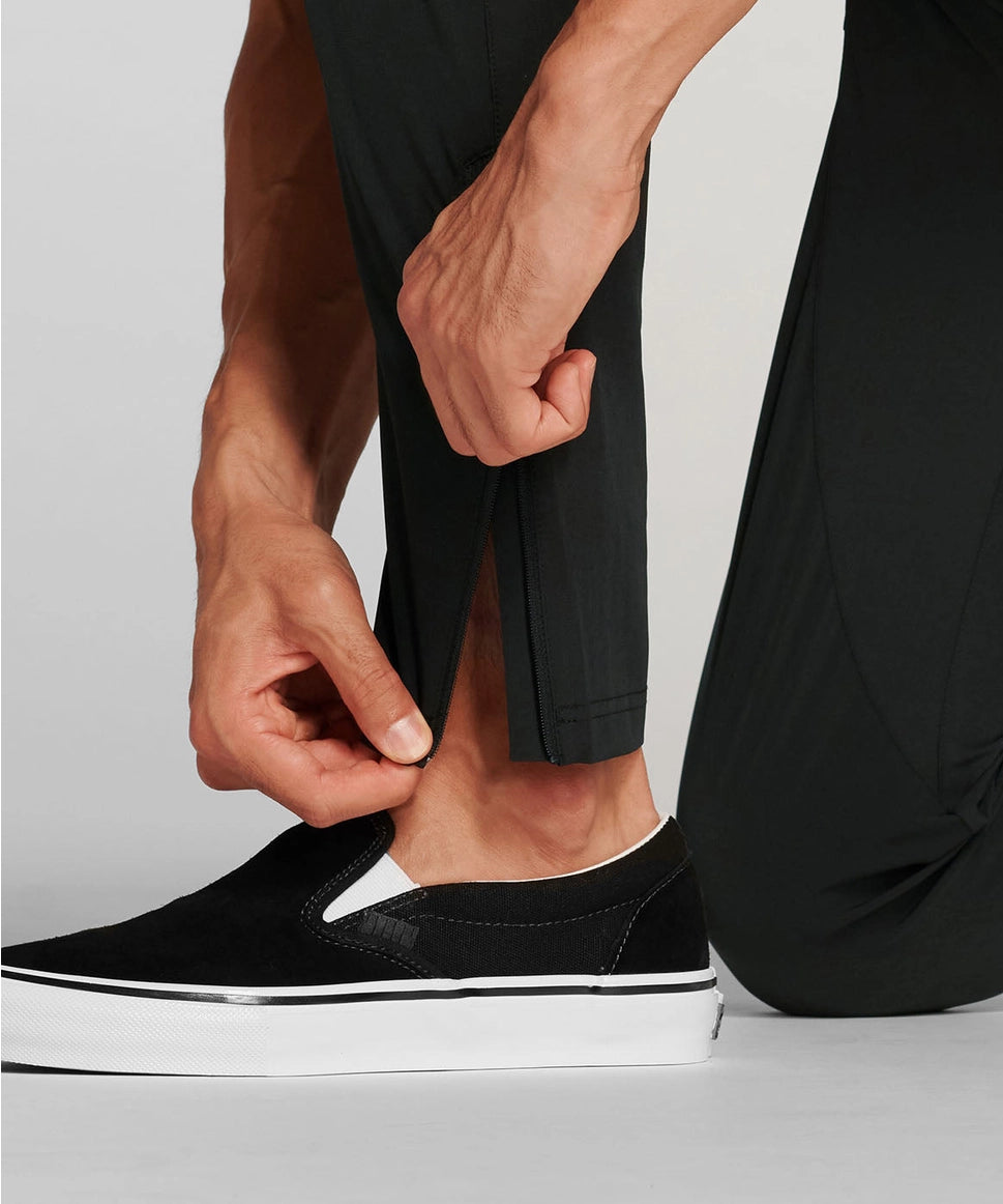 Man wearing a black slip-on shoe with a white sole on a light gray background RYU