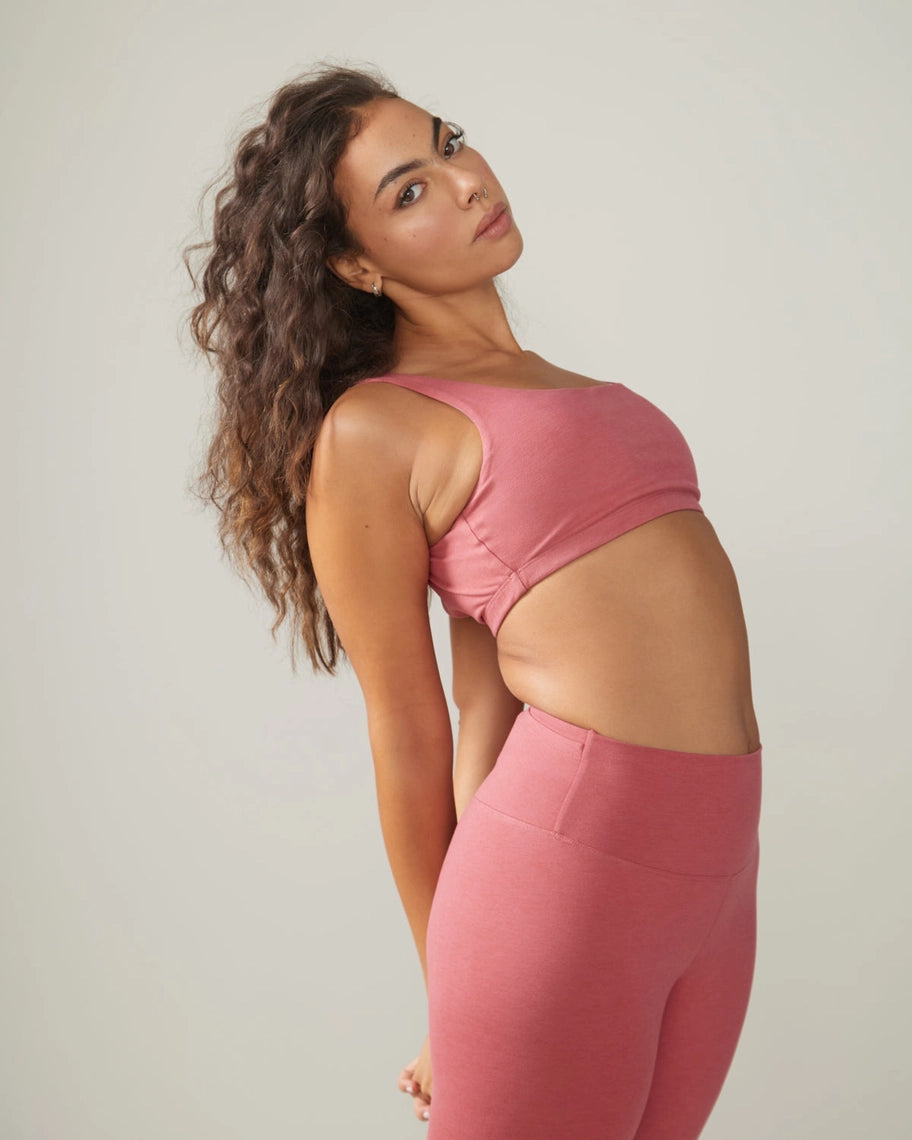 Woman in Rose Boreal pink athletic wear and cap standing outdoors with greenery in the background