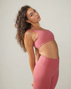 Woman in Rose Boreal pink athletic wear and cap standing outdoors with greenery in the background