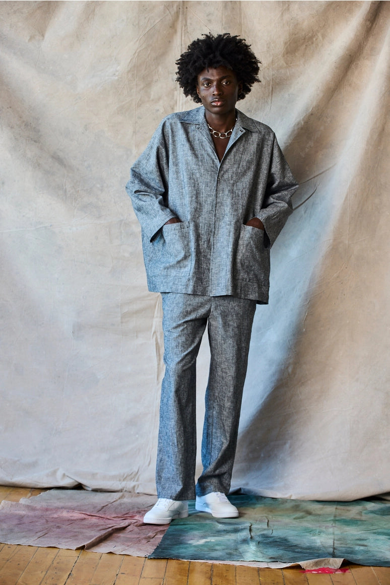 Man wearing a gray outfit standing against a textured beige wall. Devlyn van Loon