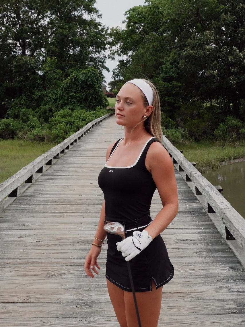 Woman in black athletic wear holding a golf club on a wooden bridge