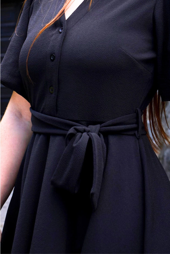 Black dress with a tie waist worn by a women. ANNICK