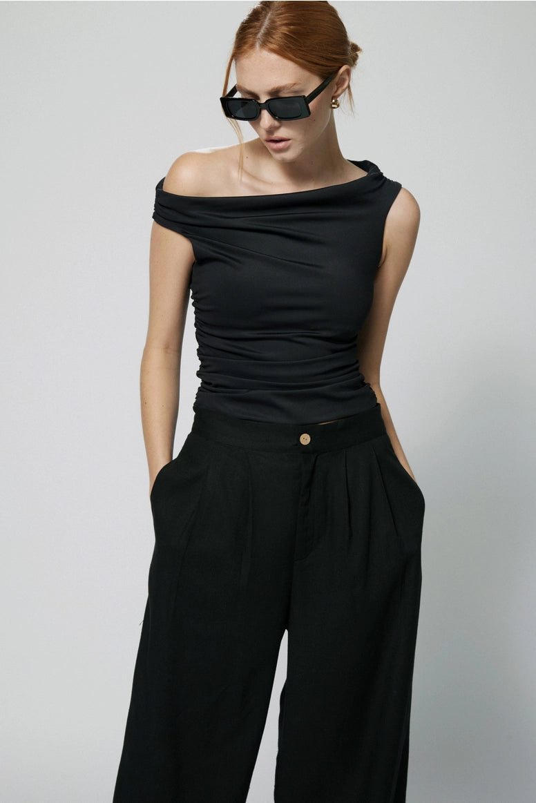 Woman wearing a black off-shoulder top and wide-leg pants against a plain background Amanda Maria