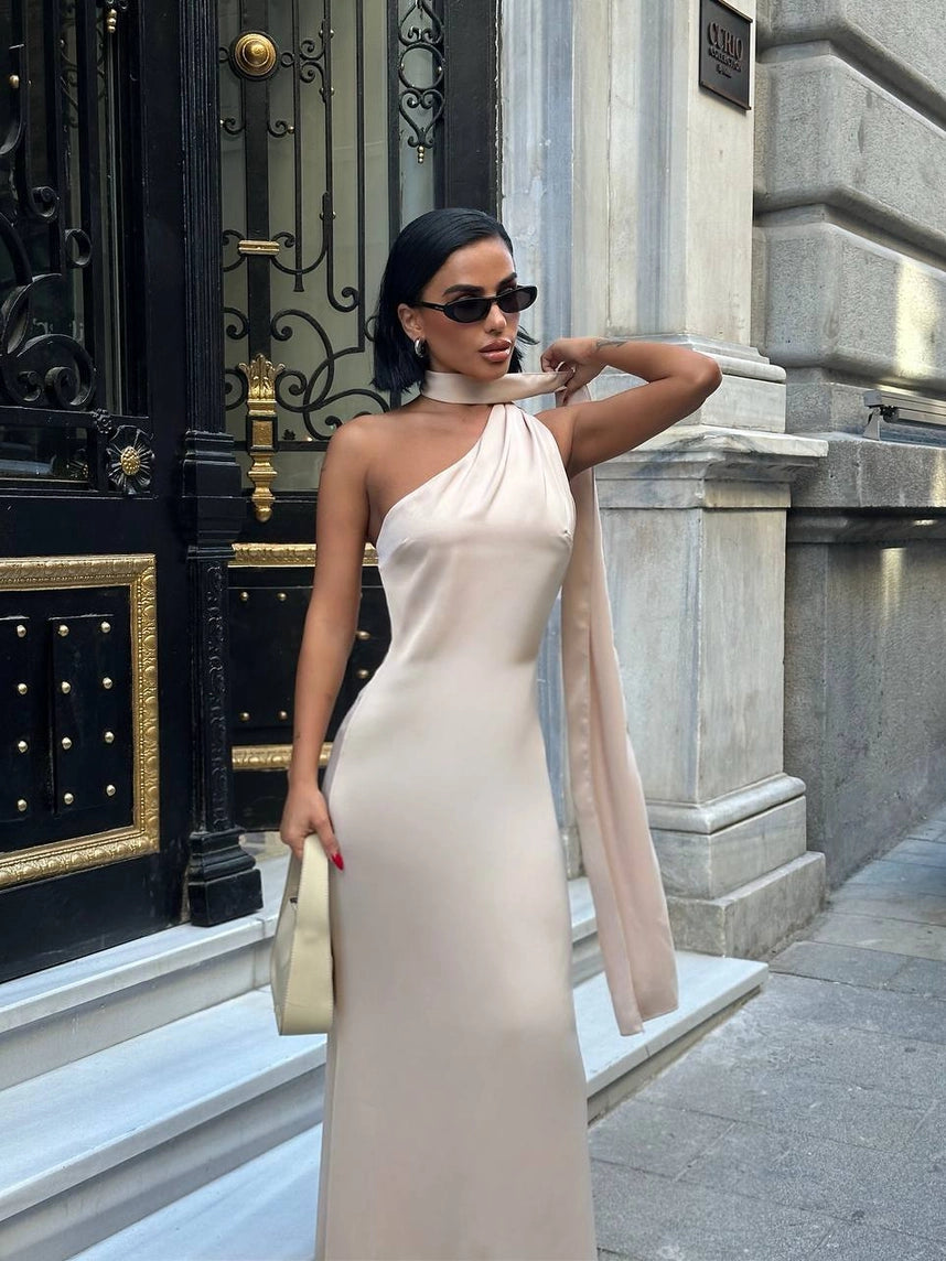 Woman in a white one-shoulder dress standing in front of a building entrance. Standpoint Top