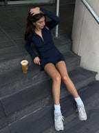 Woman sitting on steps wearing a dark blue BOV Active dress and white sneakers, with a coffee cup beside her.