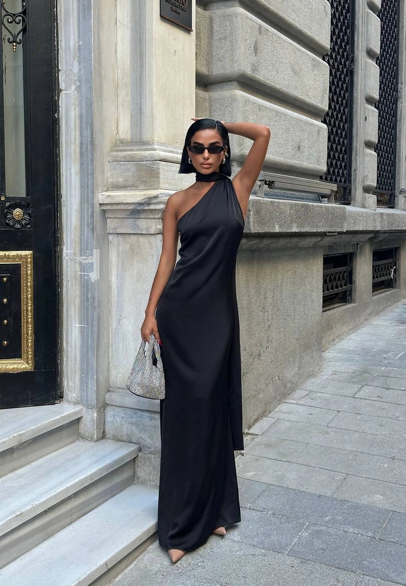 Woman in a black one-shoulder dress standing on a city street. Standpoint Top