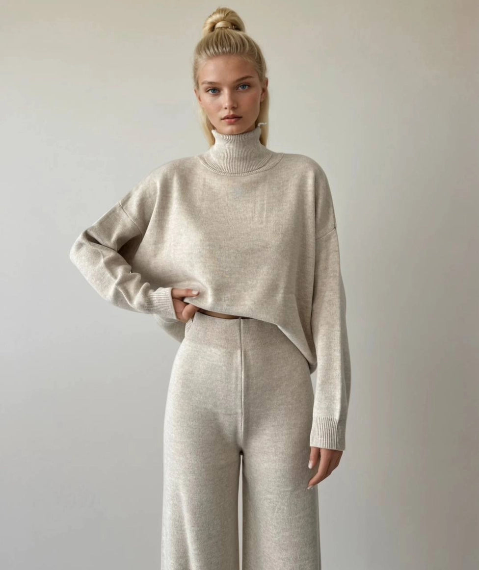 Woman wearing a beige turtleneck sweater and pants against a plain background Anaz