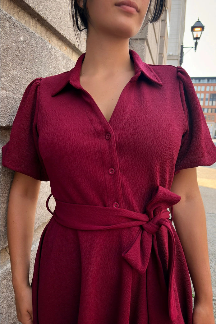 Red dress worn by a person against an urban background ANNICK