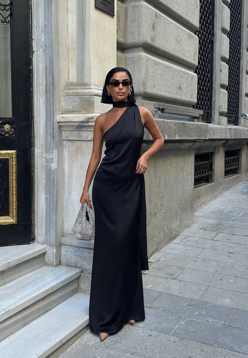 Woman in a black one-shoulder dress standing on a city street. Standpoint Top