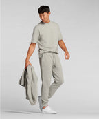 Man wearing a gray t-shirt and pants holding a jacket on a plain background RYU