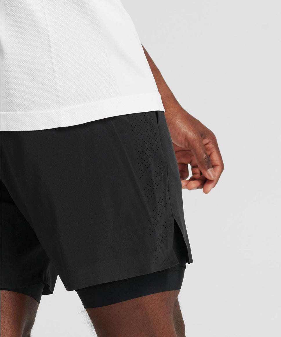 Man wearing black athletic shorts over a white shirt on a light gray background RYU