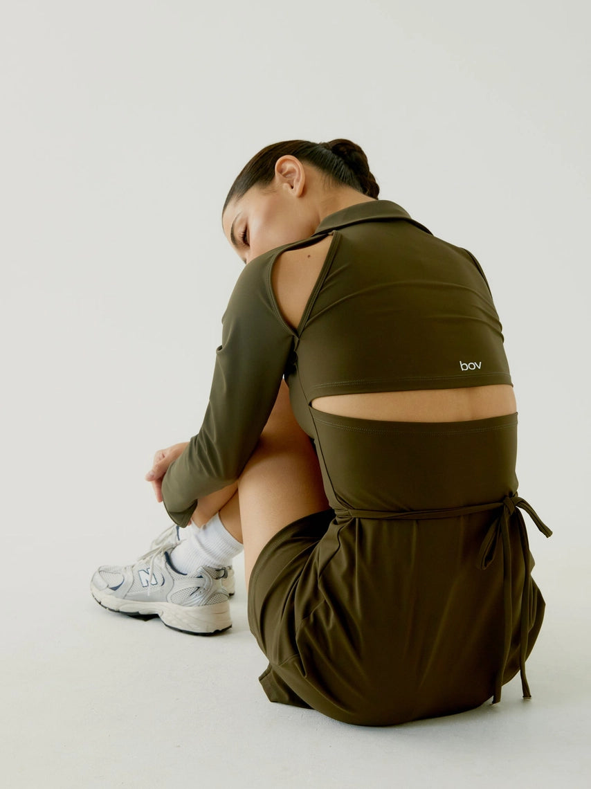 Women wearing a BOV Active green backpack sitting on the floor with a plain background