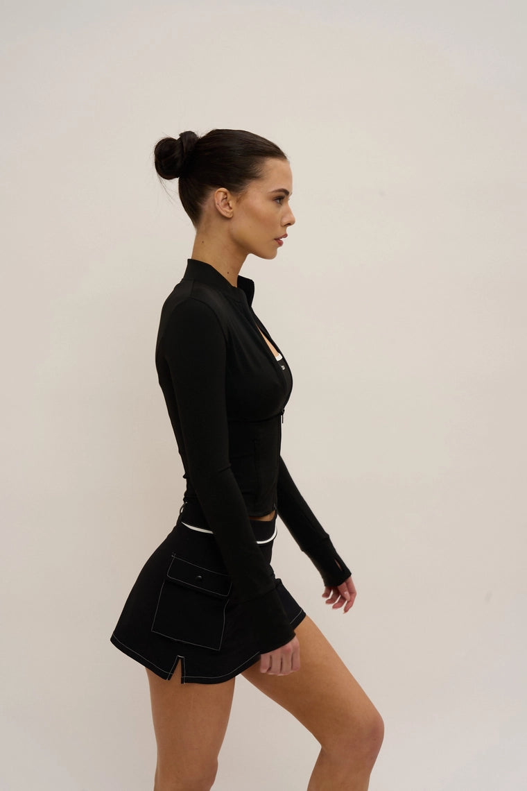Woman wearing a black outfit with a high collar and skirt on a plain background