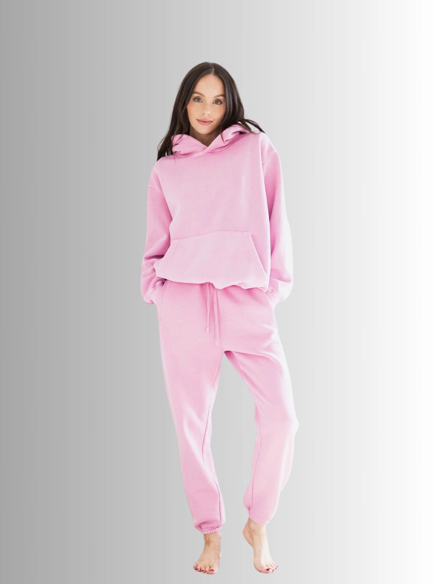 Woman wearing a pink hoodie and pants set on a gray background PRIV