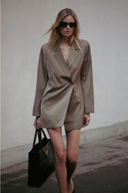 Woman in a beige suit holding a black handbag against a plain background  Amanda Maria