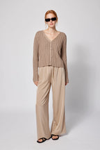 Woman wearing a beige cardigan and pants with sunglasses on a white background Amanda Maria