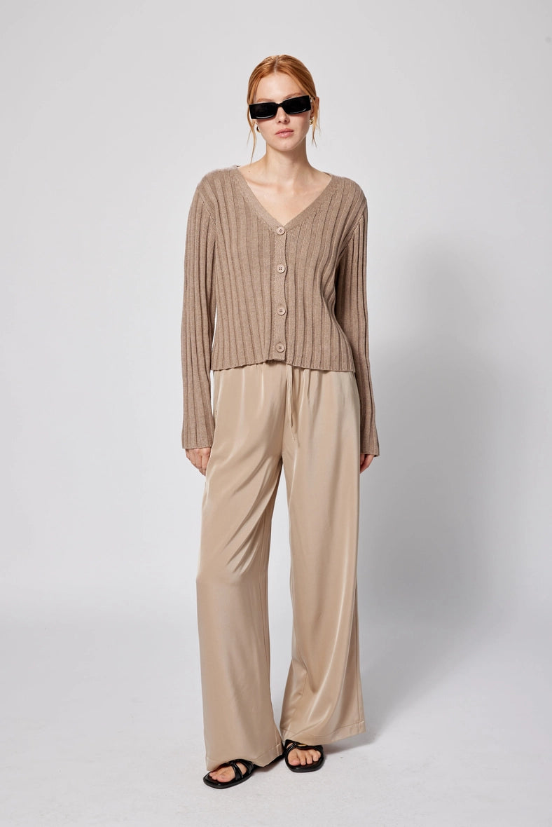 Woman wearing a beige cardigan and pants with sunglasses on a white background Amanda Maria