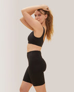 Woman in Rose Boreal black athletic wear and cap standing outdoors with white in the background