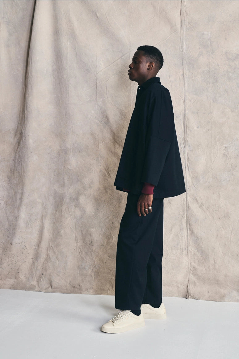Person wearing a black outfit standing against a textured beige wall. Devlyn van Loon 

