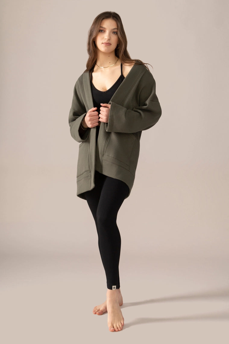 Woman wearing rose boreal  green cardigan over a black top and leggings on a beige background