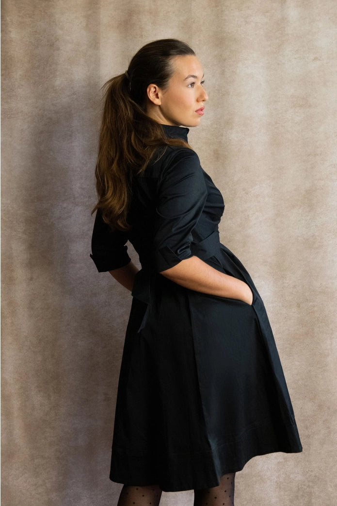Woman wearing a black dress against a textured beige background ANNICK
