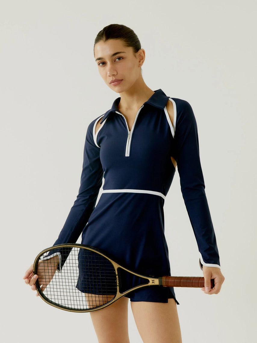 Woman in a BOV Active navy blue tennis dress holding a squash racket against a plain background