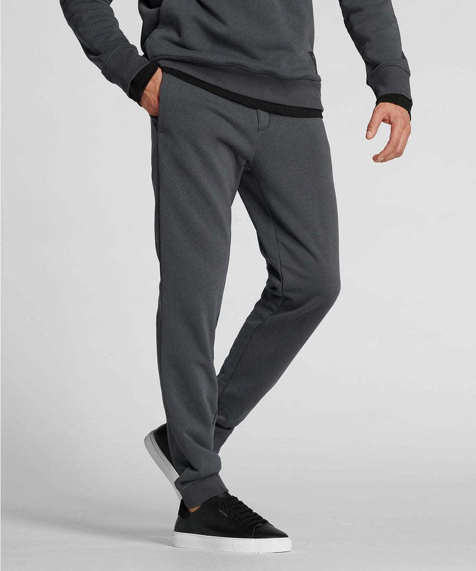 Man wearing gray sweatpants and black sneakers on a light gray background RYU