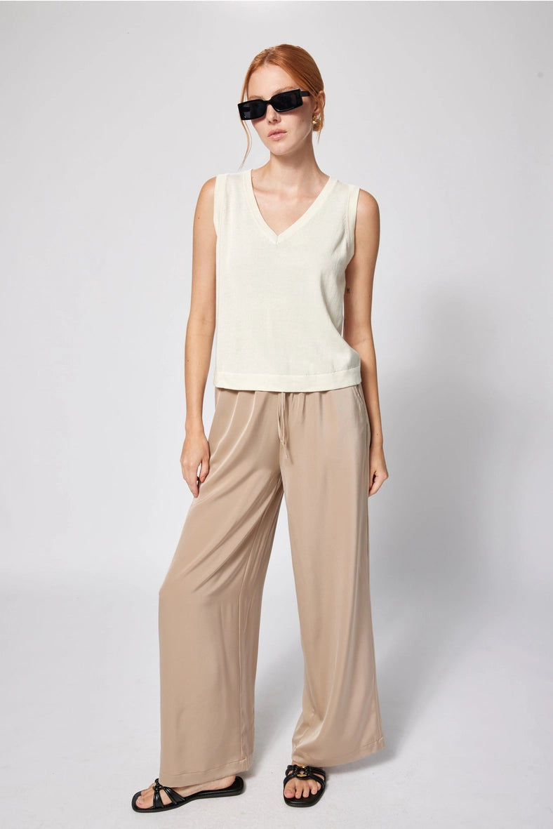 Woman wearing a white sleeveless top and beige pants against a plain background Amanda Maria