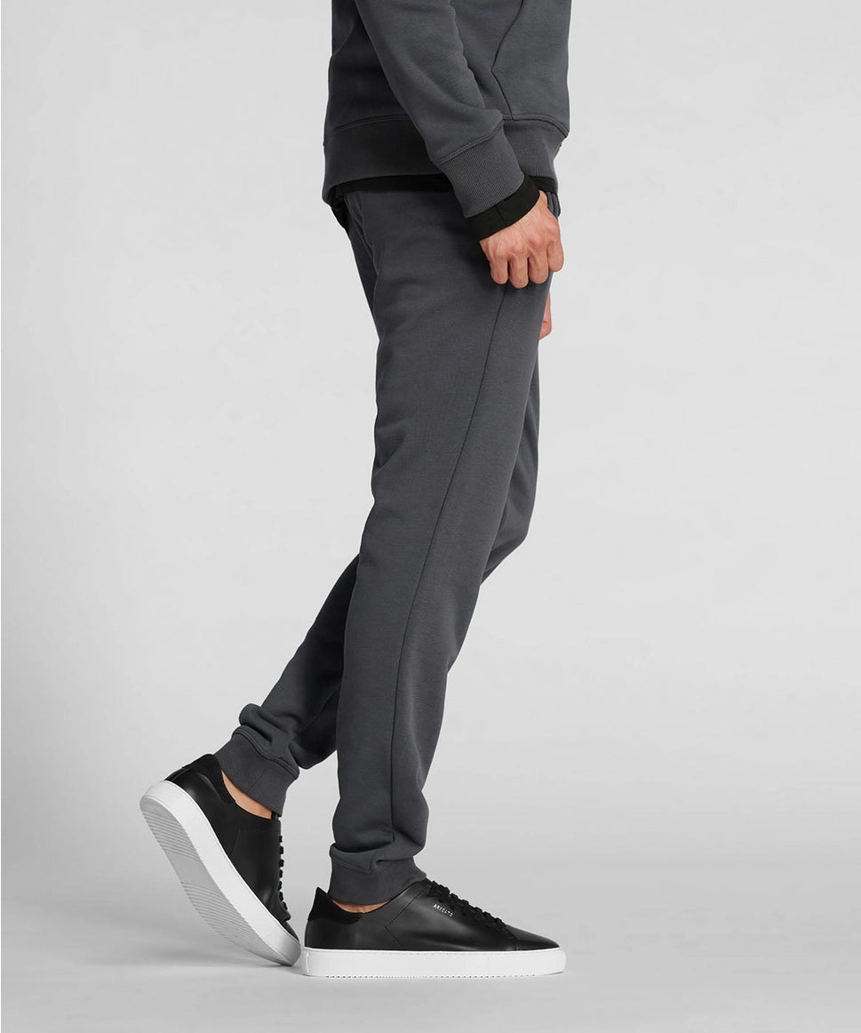Man wearing gray sweatpants and black sneakers on a light gray background RYU