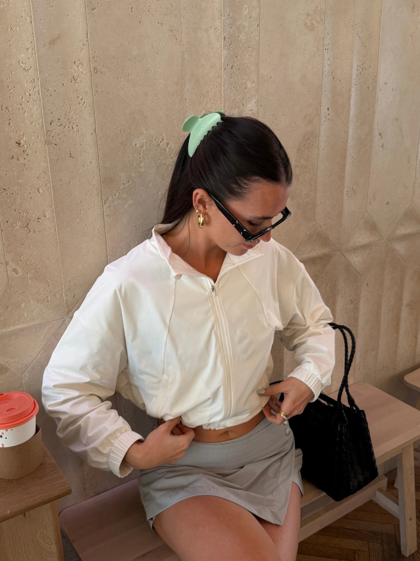 Woman in a white blouse and gray skirt sitting on a bench with a beige wall background