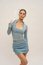 Woman in light blue athletic outfit holding a tennis racket against a plain background