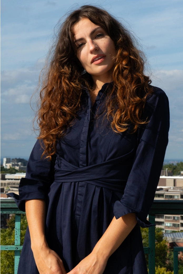 Woman wearing a navy blue dress with a cityscape in the background ANNICK