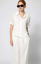 Woman wearing a white outfit with sunglasses on a plain background Amanda Maria