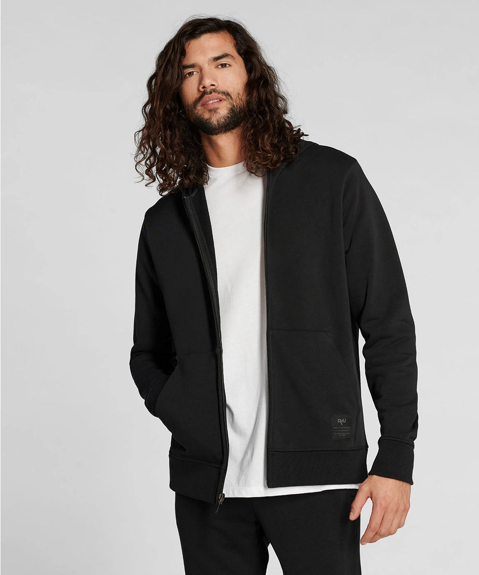 Man wearing a black jacket over a white shirt on a light gray background RYU