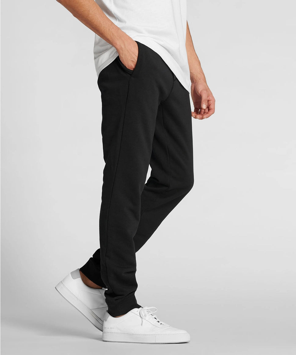 Man wearing black pants and white sneakers on a light gray background RYU