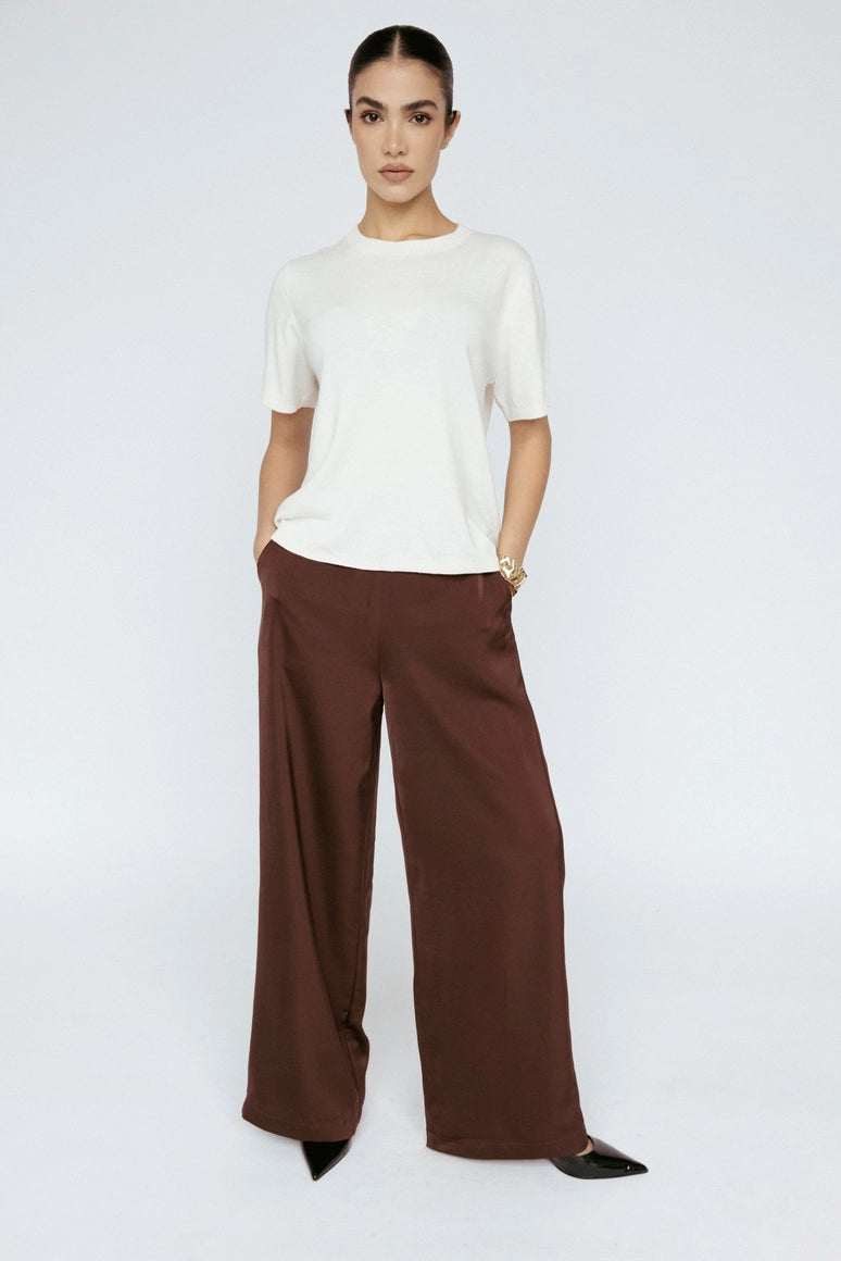 Person wearing a white top and brown wide-leg pants on a white background Amanda Maria