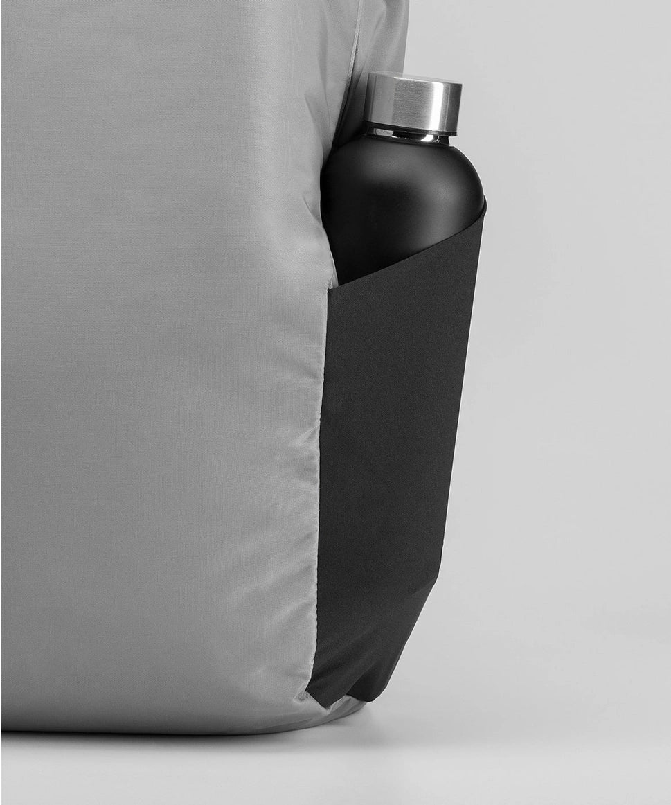 Black water bottle with silver cap inside a gray backpack pocket on a light gray background RYU
