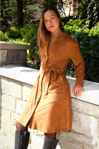 Woman wearing a brown suede dress standing outdoors with greenery in the background ANNICK