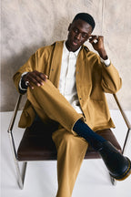 Man in a mustard jacket and pants sitting on a chair against a neutral background Devlyn van Loon 