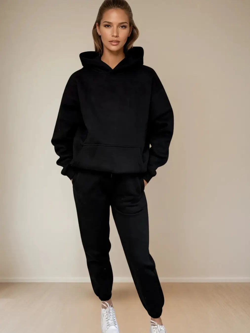 Women wearing a black hoodie and black pants with white sneakers against a beige background PRIV