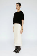 Woman wearing a black top and white skirt on a white background Amanda Maria