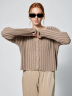 Woman wearing a beige ribbed cardigan and sunglasses against a plain background Amanda Maria