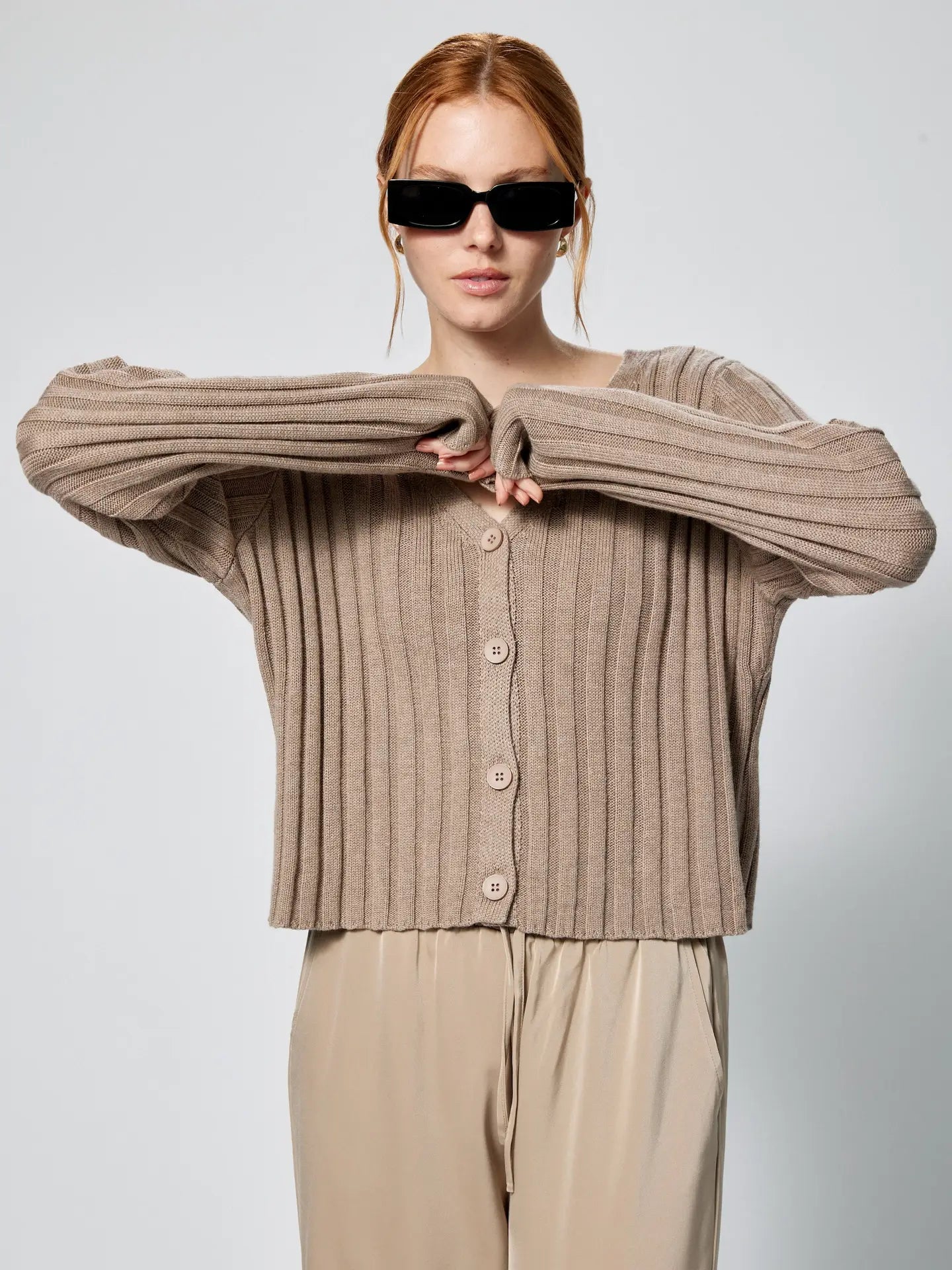 Woman wearing a beige ribbed cardigan and sunglasses against a plain background Amanda Maria
