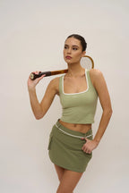 Woman in green athletic wear holding a tennis racket against a plain background